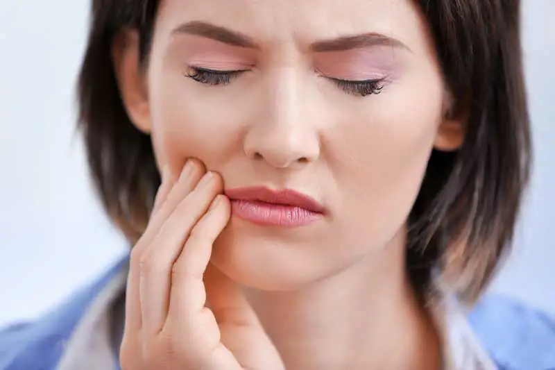 A woman holding the side of her mouth with a painful look on her face.