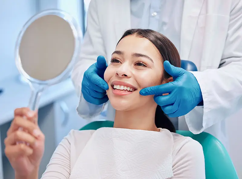 A patient smiling in a dentist chair holding up a mirror at Duggan Endodontics