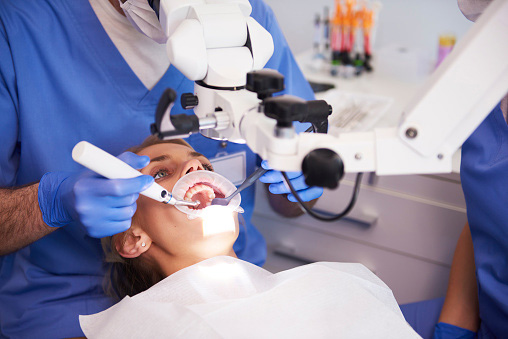 Young woman laying in dental chair while an endodontist inspects her teeth.