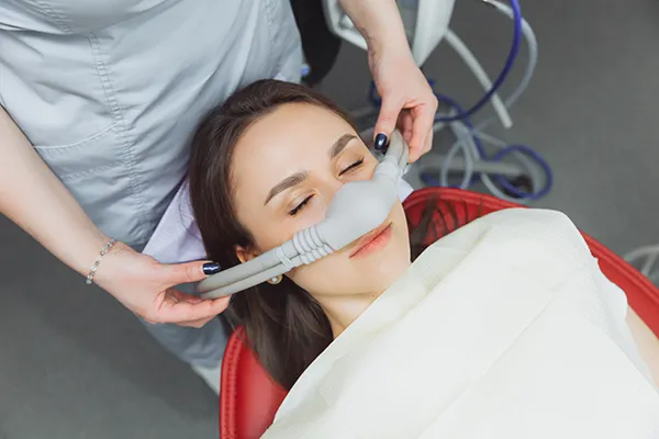 Dental assistant fitting a sedation mask over the nose of her calm female patient.