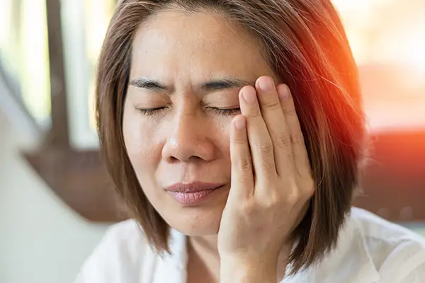 A woman holding her jaw in discomfort, showing symptoms of TMJ pain with a look of distress.